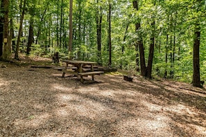 A forested area with a wooden picnic table surrounded by trees. - Camper Cabin Escape with Fire Pit and Covered Porch in Branson, Missouri (Branson)