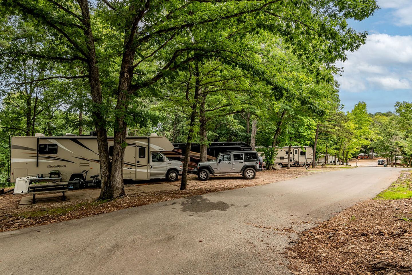 A campground with RVs parked along a paved road, surrounded by trees.