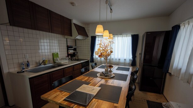 Une cuisine moderne avec un îlot en bois, une table à manger avec des sets de table et un vase contenant des fleurs séchées.