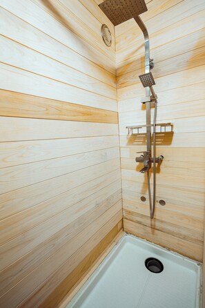 Un cerramiento de ducha con paneles de madera, un cabezal de ducha, una ducha de mano y un estante pequeño.
