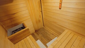 Un sauna en bois, avec un banc, une petite ouverture pour les copeaux de bois et un thermomètre fixé au mur.