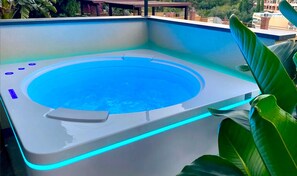 Ein Whirlpool im Freien mit blau beleuchtetem Rand, umgeben von viel Grün.