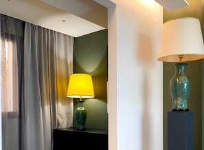 Una habitación con una cama, una mesita de noche, una lámpara y una cortina.
