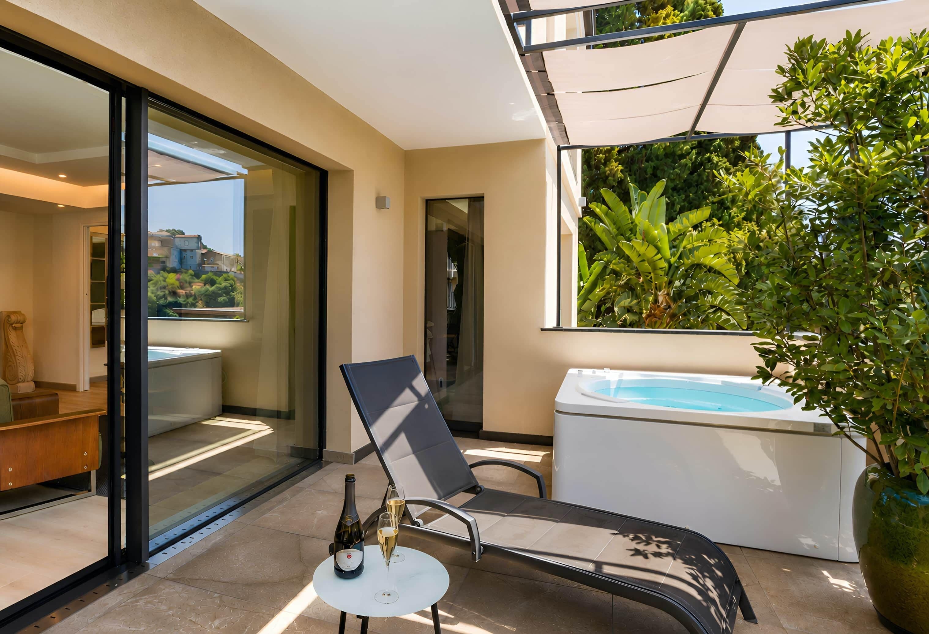 A modern outdoor area with a glass door leading to a pool, a lounge chair, a small table with a bottle and glass, and a large potted plant.
