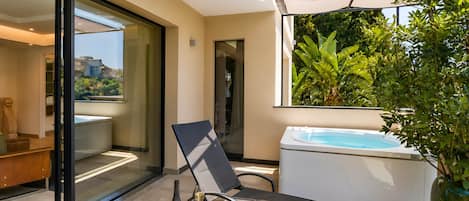 Un espacio exterior moderno con puerta de cristal que da a una piscina, una silla de descanso, una pequeña mesa con una botella y un vaso, y una planta grande en maceta.