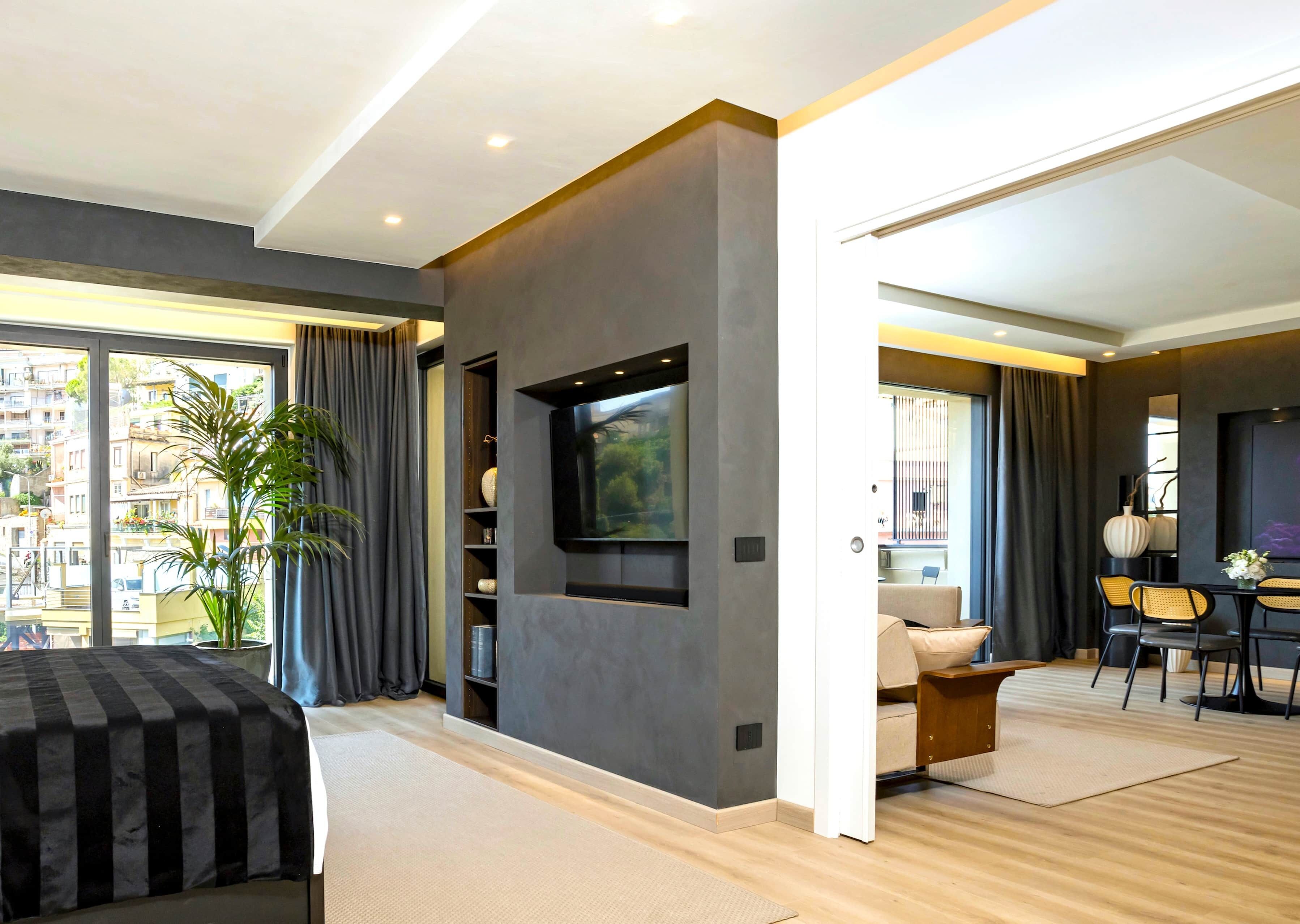 Una camera d'albergo moderna con un letto grande, una televisione a schermo piatto montata a parete, un'area pranzo con tavolo e sedie e vista sulla città attraverso ampie finestre.