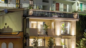 Un edificio residencial de varios pisos con balcones, ventanas amplias y un árbol en primer plano.