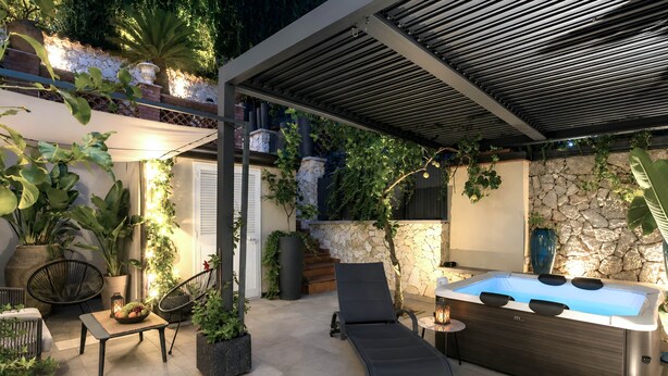 Un patio al aire libre con un jacuzzi, sillones de descanso y plantas en macetas.