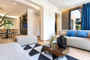 A modern living room with a sofa, ottoman, coffee table, and a dining area with chairs and a table. - Alba Suite-Taormina In Light Suite (Taormina)