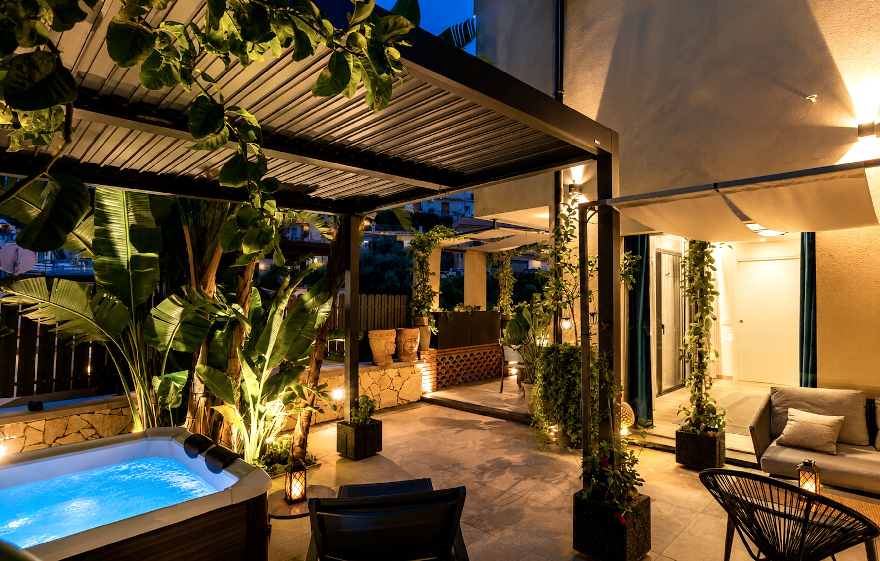 An outdoor patio area with a hot tub, seating, and potted plants.