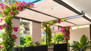 Un espacio al aire libre cubierto con una pérgola, plantas en macetas y vistas a edificios cercanos.