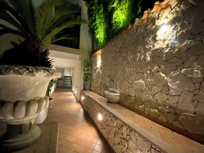 A corridor with a stone wall, a water feature, and a large potted plant. - Alba Suite-Taormina In Light Suite (Taormina)