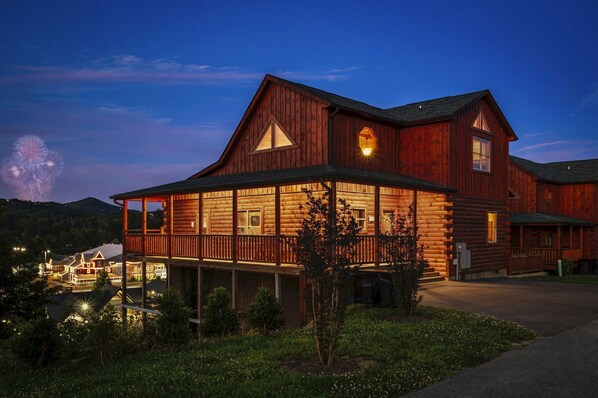 A large wooden building with a covered porch, multiple windows, and a well-lit entrance. - Family Cabin with Indoor Pool, Hot-Tub and Pool Table in Tennessee (Pigeon Forge)