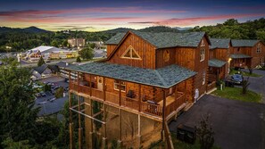 A wooden cabin with a balcony, surrounded by a parking lot and other buildings. - Family Cabin with Indoor Pool, Hot-Tub and Pool Table in Tennessee (Pigeon Forge)