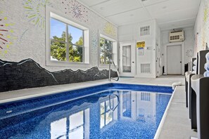 An indoor swimming pool with clear windows, a caution sign, and a door leading to another room. - Family Cabin with Indoor Pool, Hot-Tub and Pool Table in Tennessee (Pigeon Forge)