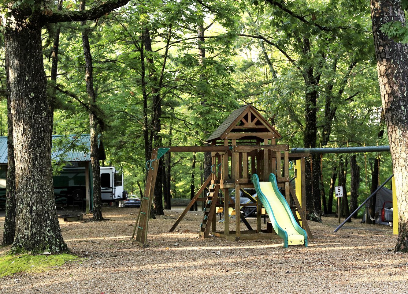 A playground with a wooden structure, a slide, and a speed limit sign.