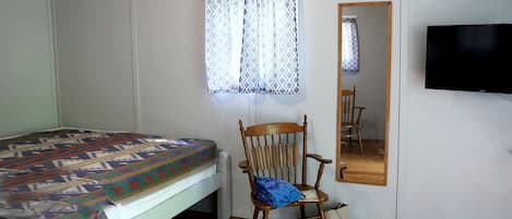 Una habitación con cama, una silla, un espejo y televisor.