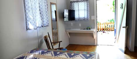 Une chambre à coucher comprenant un lit, une chaise, un bureau, un téléviseur et une porte donnant sur l’extérieur.