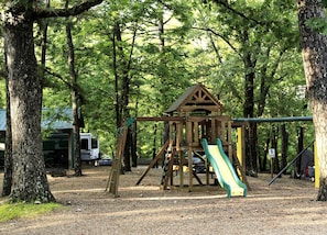 A playground with a wooden structure, a slide, and a speed limit sign. - Rustic Camper Retreat with Fire Pit & Rocking Chairs in Branson, Missouri (Branson)