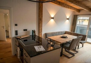A modern kitchen with a central island, a dining area with a wooden table and chairs, and a large window providing natural light. - Haus3310 by we rent (Bad Hofgastein)