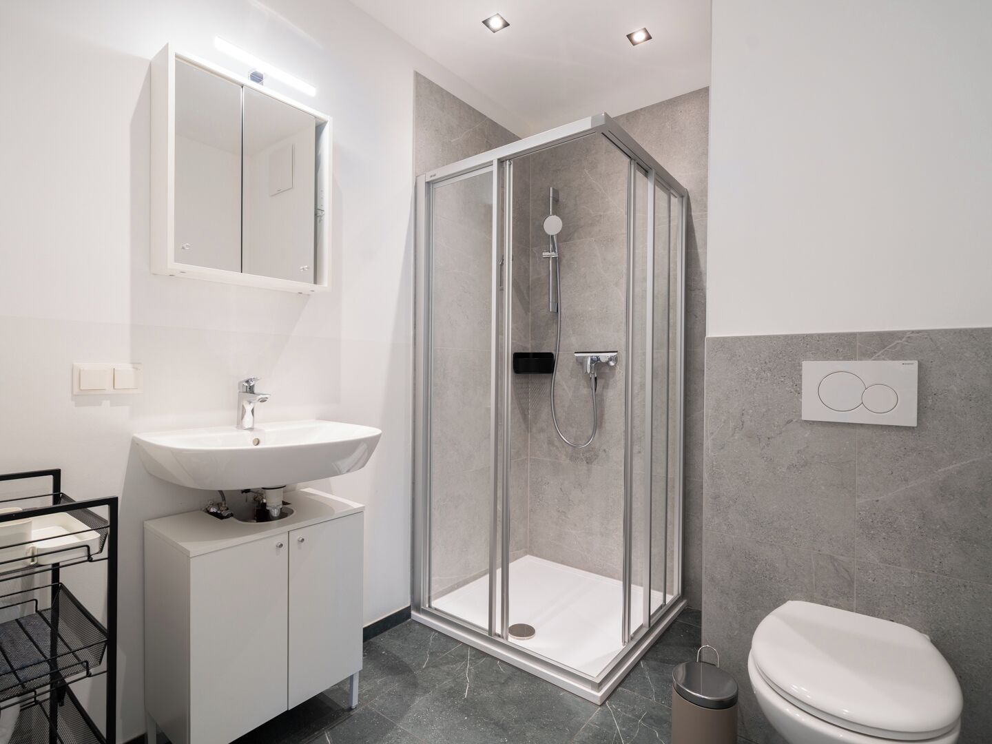 A modern bathroom with a glass-enclosed shower, a white sink, and a toilet.