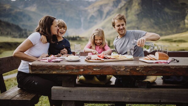 A family dining outdoors with a mountainous backdrop. - Haus3310 by we rent (Bad Hofgastein)