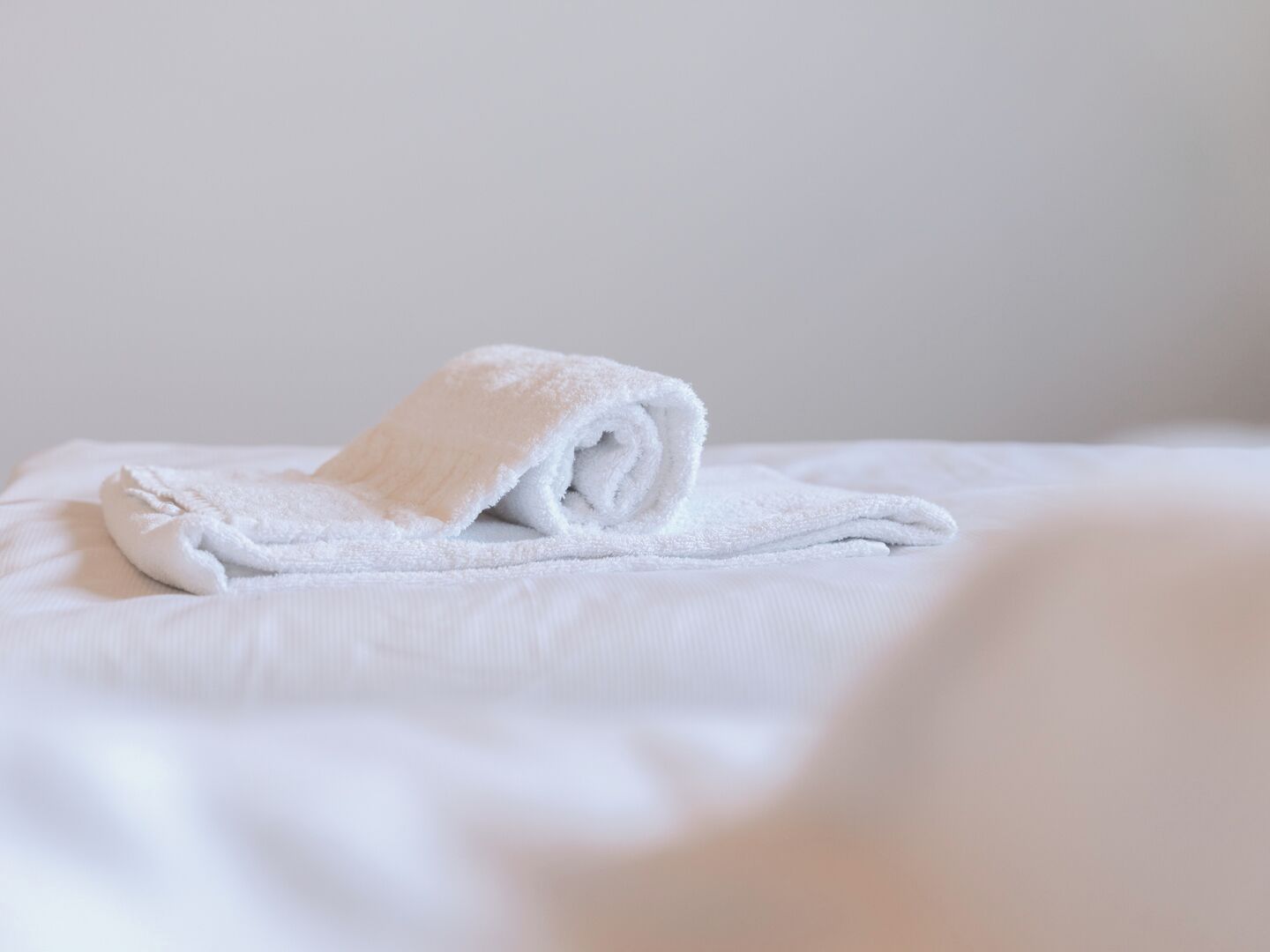 Une serviette blanche, soigneusement pliée, est posée sur un lit, le fond étant uni.