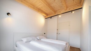 A bedroom with a wooden ceiling, a white bed with two pillows, and a door. - Haus3310 by we rent (Bad Hofgastein)