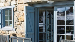 A stone building with a large glass door and a window with blue shutters.