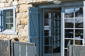 A stone building with a large glass door and a window with blue shutters.