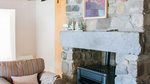 A stone fireplace with a modern stove, a striped sofa with a cushion, and a framed picture on the wall.