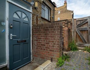 A residential property with a blue garage door, a brick wall, and a wooden gate. - Basement Flat Sleeps 3 With Patio (London)
