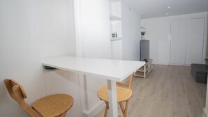 A modern, minimalistic room with a white table, two wicker chairs, a grey sofa, and a white wardrobe. - Basement Flat Sleeps 3 With Patio (London)