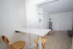 A modern, minimalistic room with a white table, two wicker chairs, a grey sofa, and a white wardrobe. - Basement Flat Sleeps 3 With Patio (London)