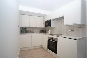 A modern kitchen with white cabinetry, a microwave, a coffee maker, and an oven. - Basement Flat Sleeps 3 With Patio (London)