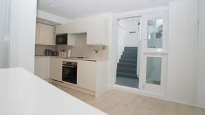 A modern kitchen with built-in appliances, a dining area, and a staircase leading to an upper level. - Basement Flat Sleeps 3 With Patio (London)
