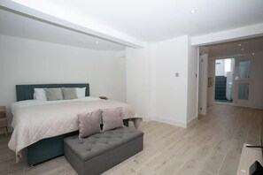 A bedroom with a bed, a bench, and a staircase. - Basement Flat Sleeps 3 With Patio (London)