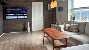 Una sala de estar moderna con piso de madera, una mesa de centro de madera, un sofá, un televisor montado en la pared y una ventana con plantas.