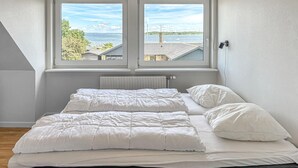 A bedroom with a large window, a bed with white bedding, and a radiator below the window. - Gorgeous apartment in Fur with house sea view (Fur)