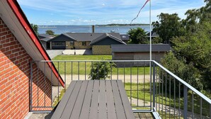 A balcony with a view of a lake, a brick building, and a wooden structure. - Gorgeous apartment in Fur with house sea view (Fur)