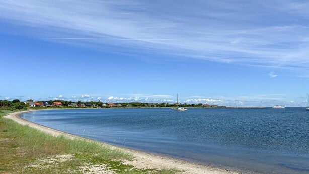 A coastal landscape with a clear sky, a sandy beach, and a distant view of a town with buildings and a bridge. - Gorgeous apartment in Fur with house sea view (Fur)