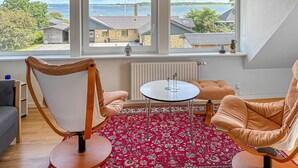 A room with a large window, a red patterned rug, two cushioned chairs, a small round table, and a radiator. - Gorgeous apartment in Fur with house sea view (Fur)