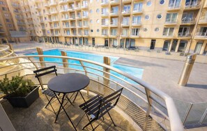Ein Balkon mit Pool, Tisch und Stühlen, mit Blick auf ein Gebäude mit mehreren Balkonen.