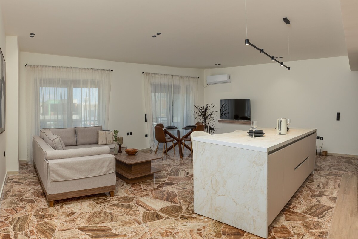 Ein modernes Wohnzimmer mit Sofa, Esstisch und Kücheninsel.