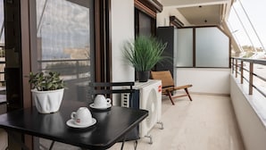 En balkon med et bord, to hvide kopper, en potteplante og en stol.