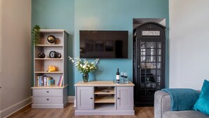 Een kamer met een boekenkast, een bureau met een bloevas, een televisie en een telefooncel.