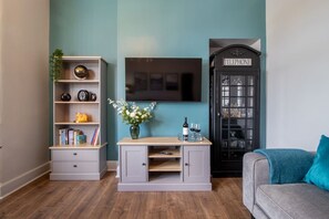Ein Zimmer mit Bücherregal, Schreibtisch mit Blumenvase, Fernseher und Telefonzelle.