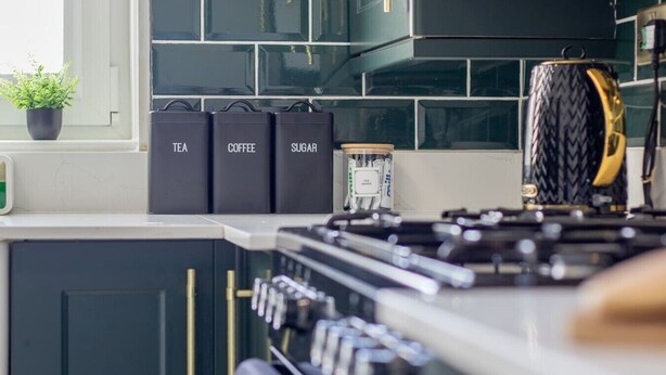 Een keuken met een fornuis, kastjes en containers met de tekst 'thee', 'koffie' en 'suiker'.