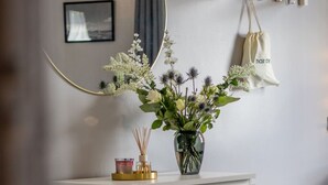 Een wit nachtkastje met een glazen vaas met witte bloemen, een kaarsje en een decoratief object.