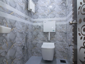A bathroom with a marble wall, a toilet, a shower, and a towel rack. - Hotel Platinum (Mumbai)
